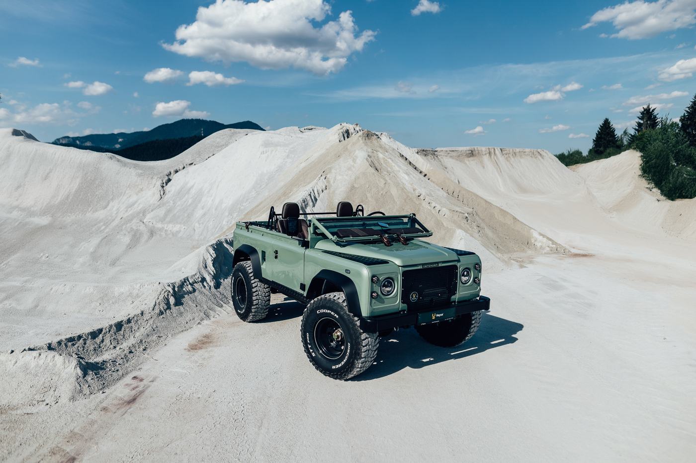 Heyus Speedster — Defender 90 so sklopeným čelným sklom a bez dverí, na bielom lome pod modrou oblohou