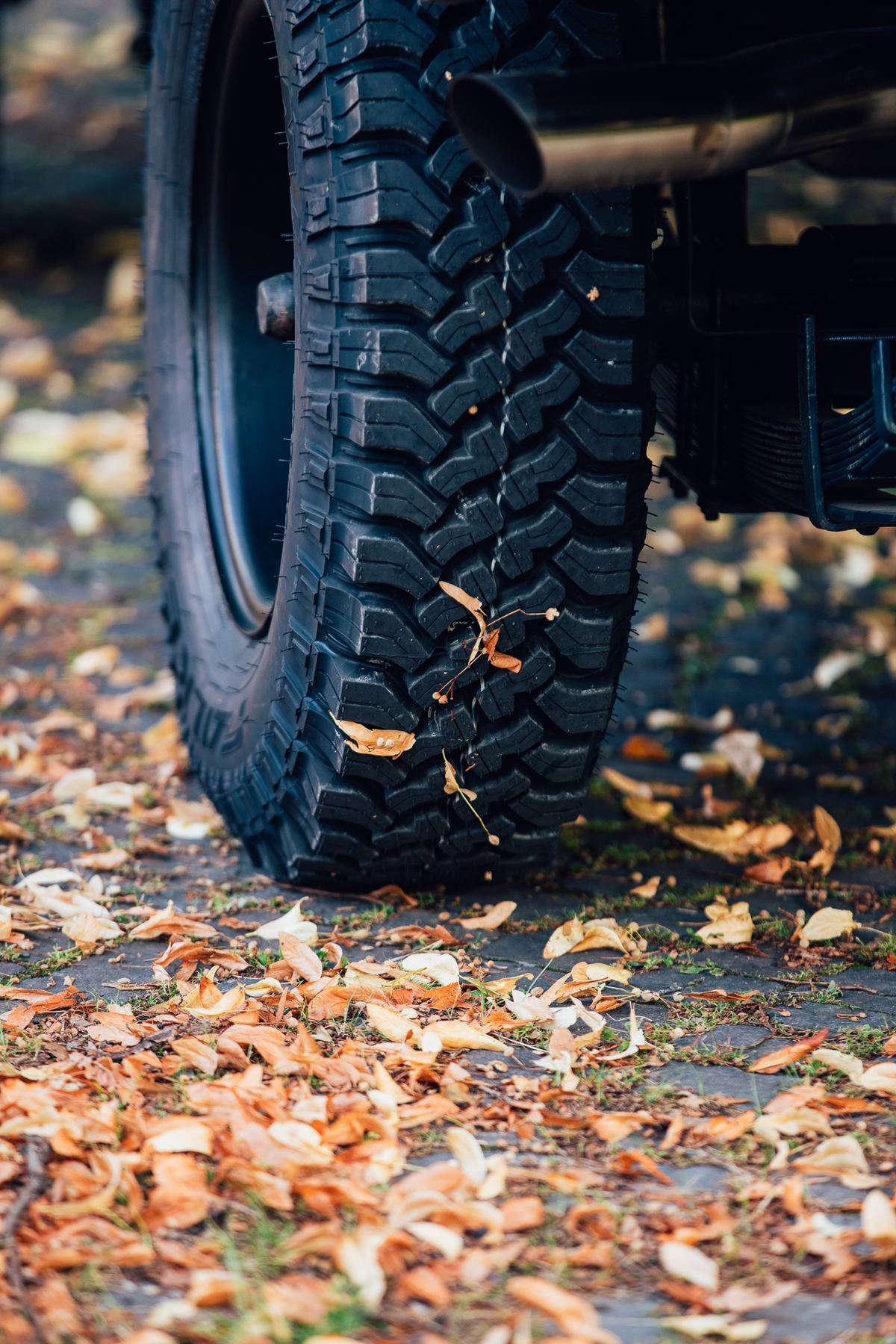A close-up, low-angle shot focuses on the rear left off-road tyre of a vehicle, likely a Land Rover given the context, parked on a cobblestone…