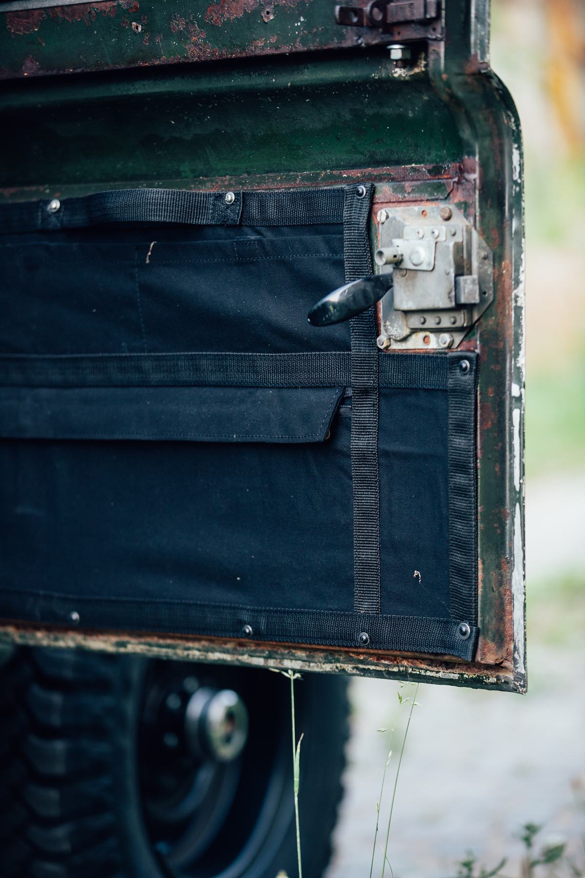 A close-up shot of the interior of an open, green vehicle door, likely from a classic Land Rover Series. The door shows significant surface rust and…