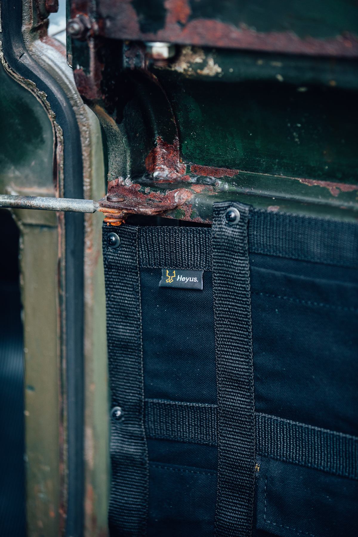 A close-up detail shot shows the interior of a dark green vehicle door, heavily rusted along its metal framework and edges. Attached to the lower…
