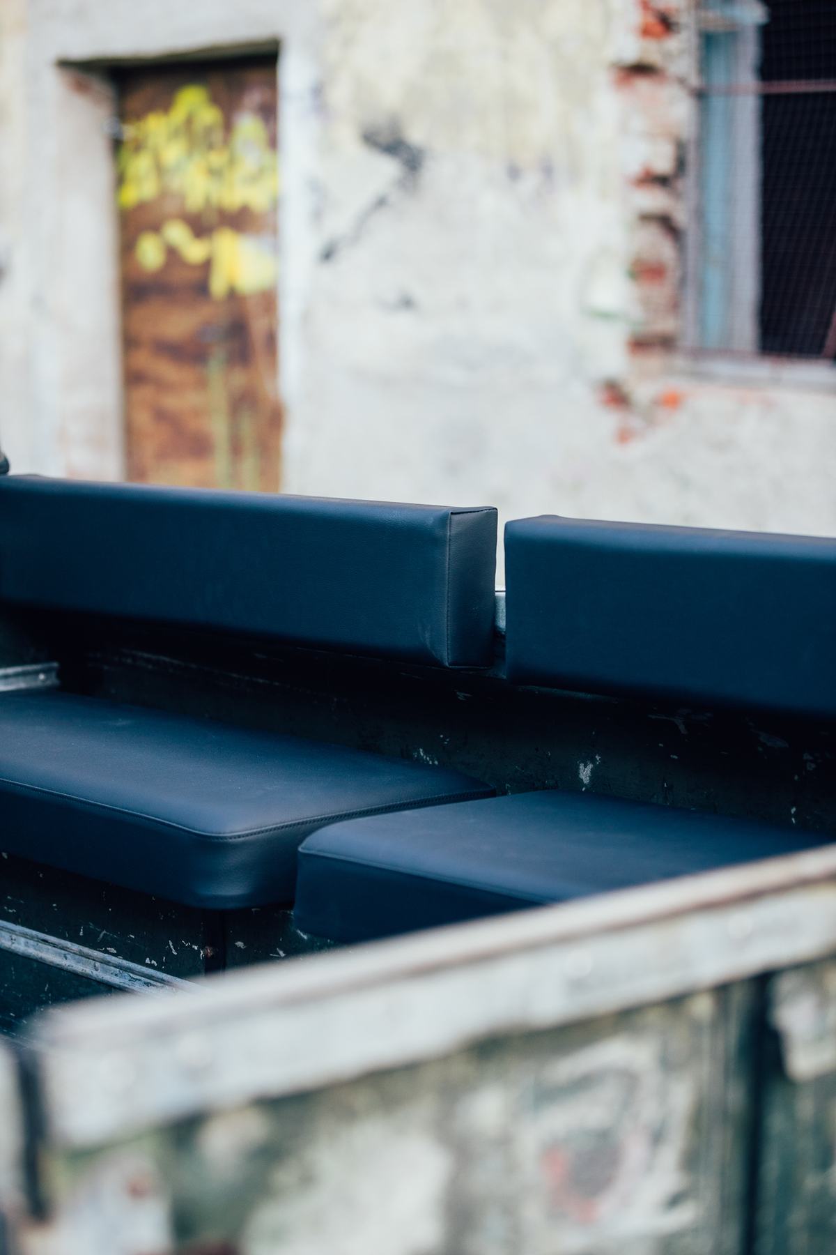 A close-up detail shot shows the rear interior of a Land Rover, focusing on two newly upholstered black vinyl seats mounted longitudinally along the…