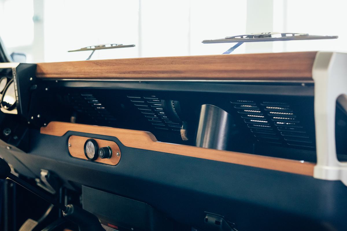 A close-up detail shot of a highly customized interior dashboard in a finished Land Rover restoration. The dash features elegant solid wood trim…